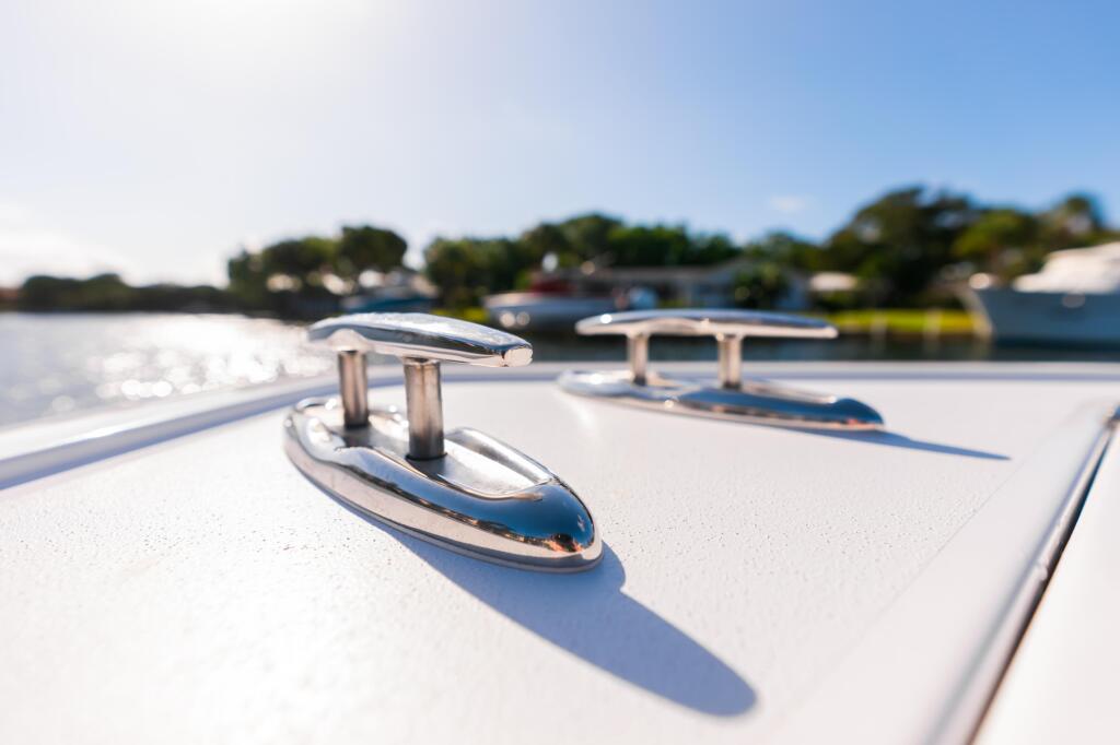 Close-up of chrome cleats and stainless steel toe rail on a boat deck with marina in background