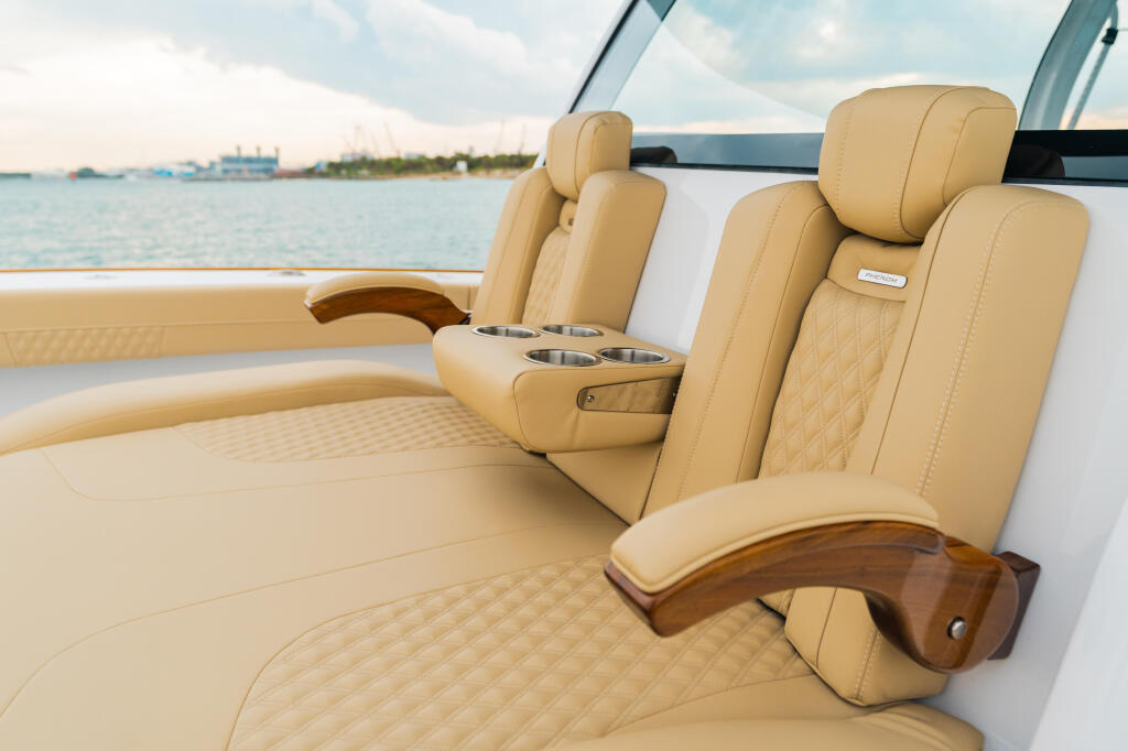 Luxury boat cabin with tan leather seating, cup holders, and wood-trimmed armrests overlooking a marina