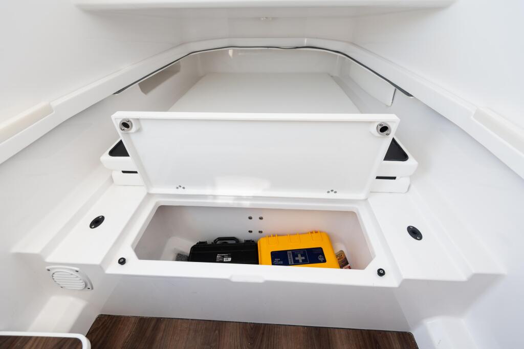 Open storage compartment in boat cabin with yellow battery and black equipment inside