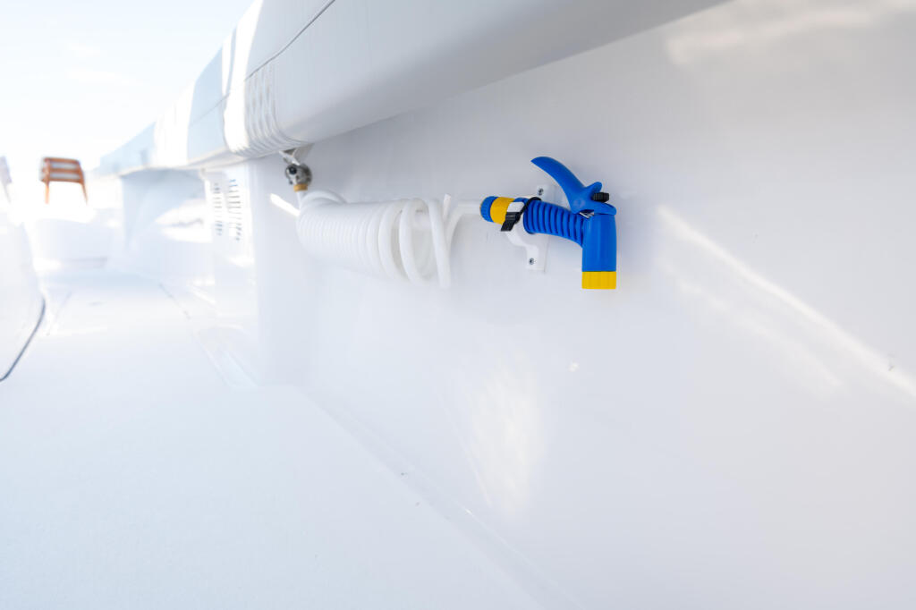 Blue and yellow freshwater spigot mounted on white boat hull with hose connection