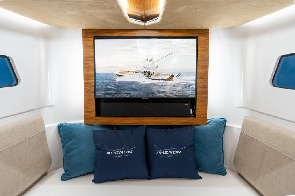 Cabin interior with 4K television displaying a fishing boat at sea, surrounded by comfortable seating and Phenom pillows