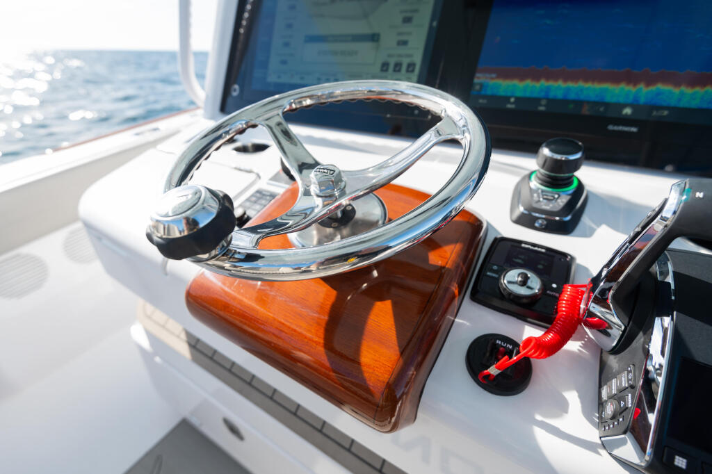 Polished chrome steering wheel with wood grain hub on boat helm, electronics and sounder visible in background