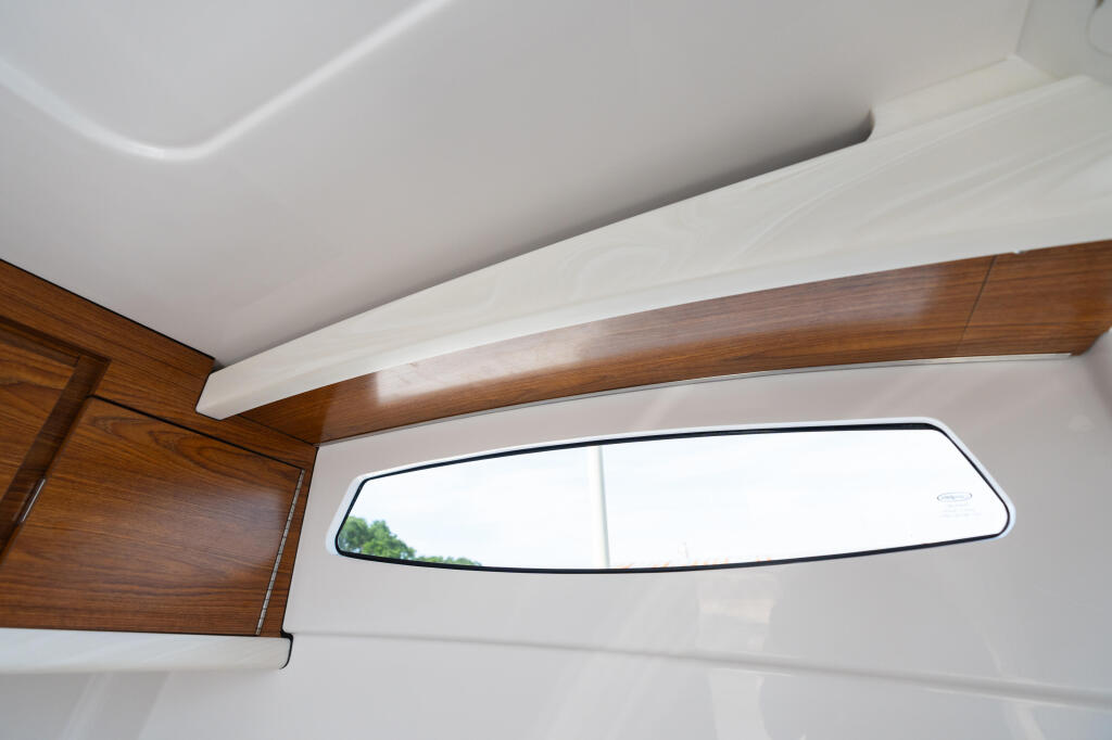 Cabin interior with wooden beam, white ceiling, and horizontal window overlooking green landscape