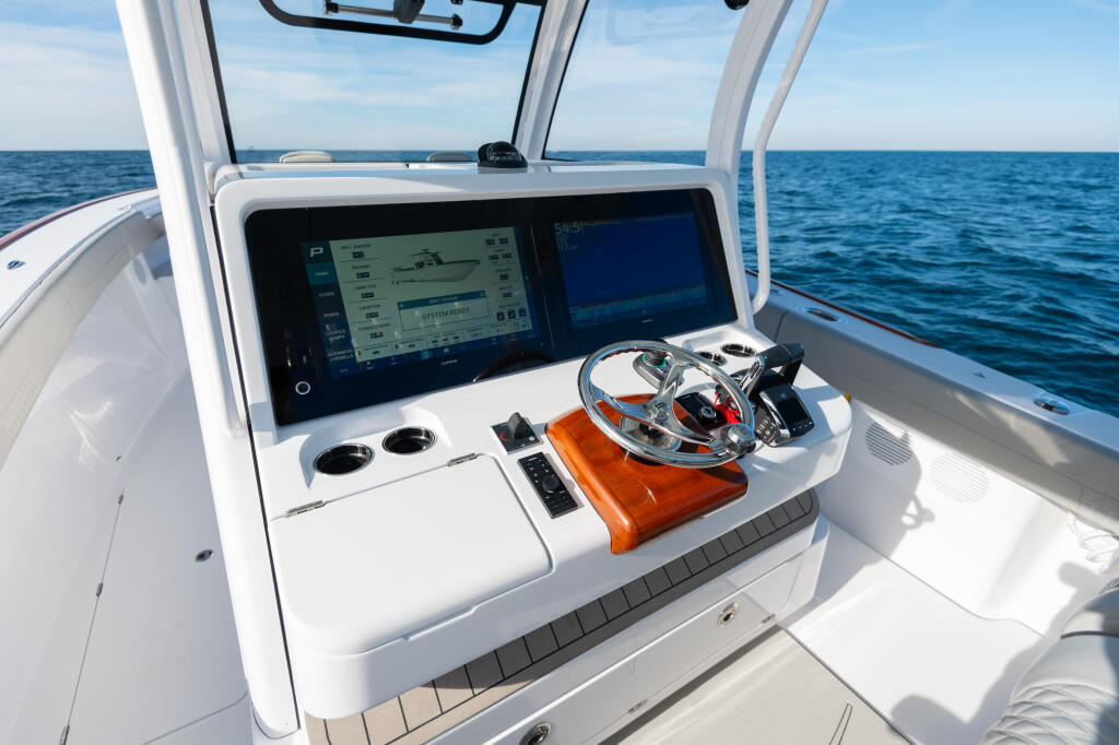 Helm station with dual touchscreen displays, chrome steering wheel, and cup holders overlooking open ocean