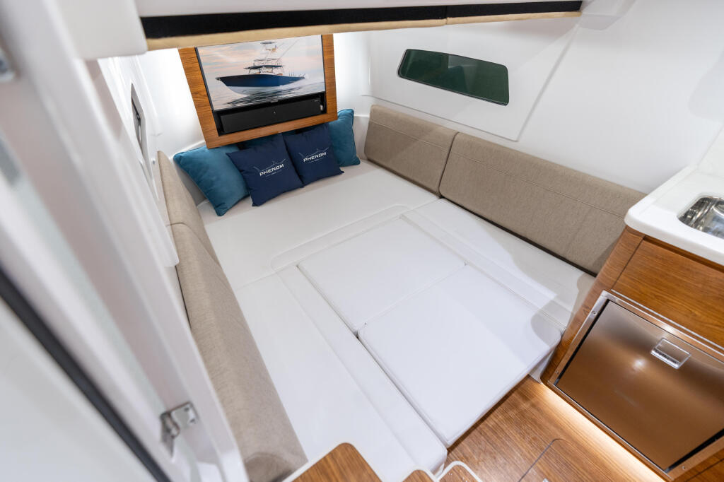 Cabin interior with convertible queen-sized bed, beige upholstered bench seating, TV, and wood accents