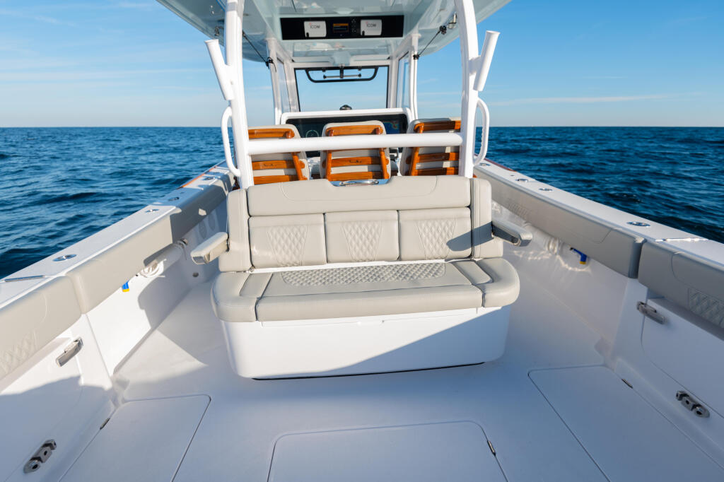Spacious rear deck with cream-colored seating, orange accent rail, and clear ocean view from fishing boat