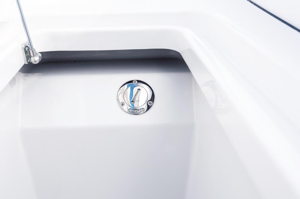 Chrome pump-out fitting with blue indicator gauge mounted on white fiberglass cabin wall
