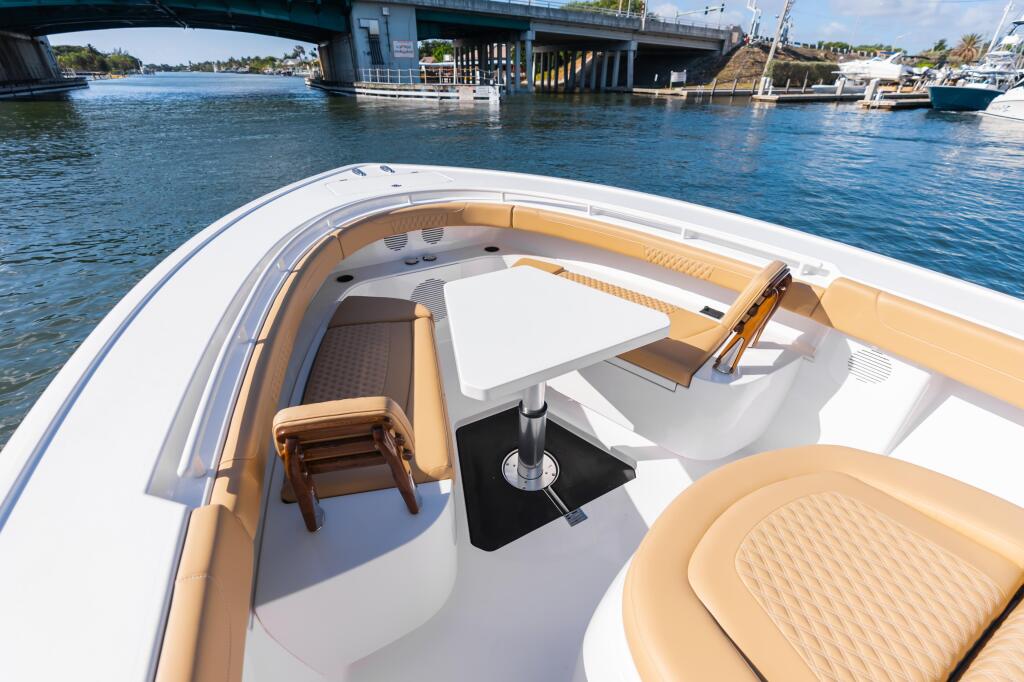 Spacious boat cockpit with tan upholstered seating, white deck, and electronically actuated bow table in a marina setting