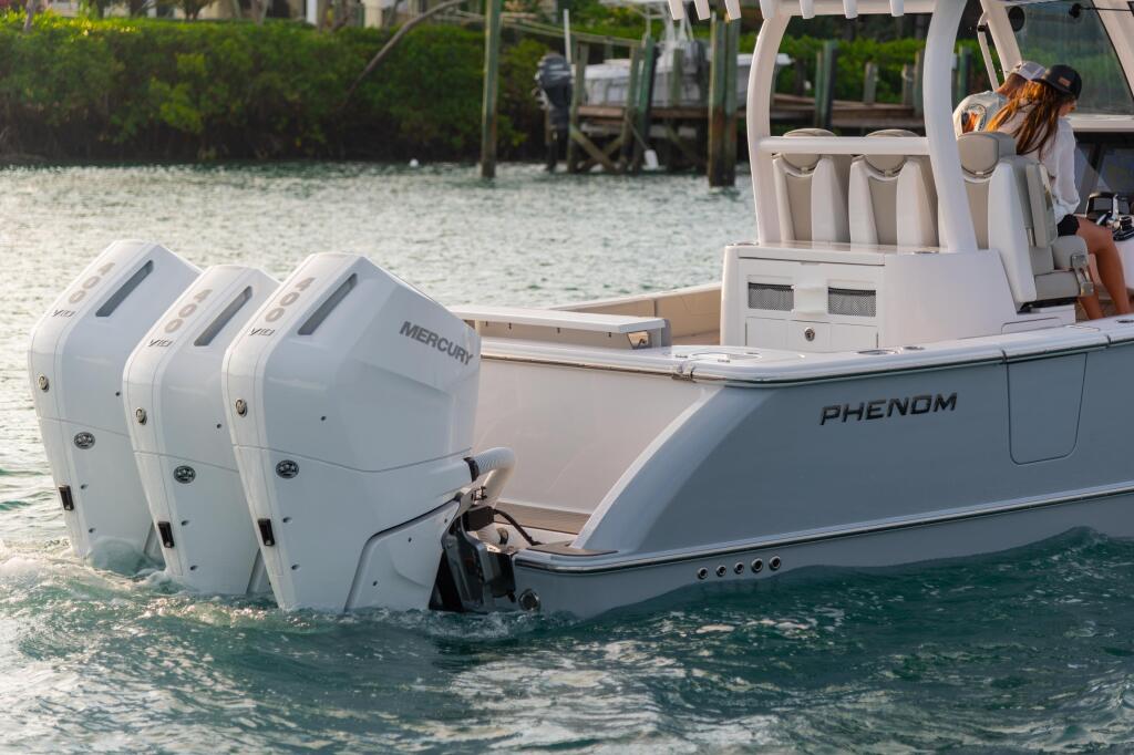 Phenom center console boat with triple Mercury engines docked at a sandy beach near mangroves