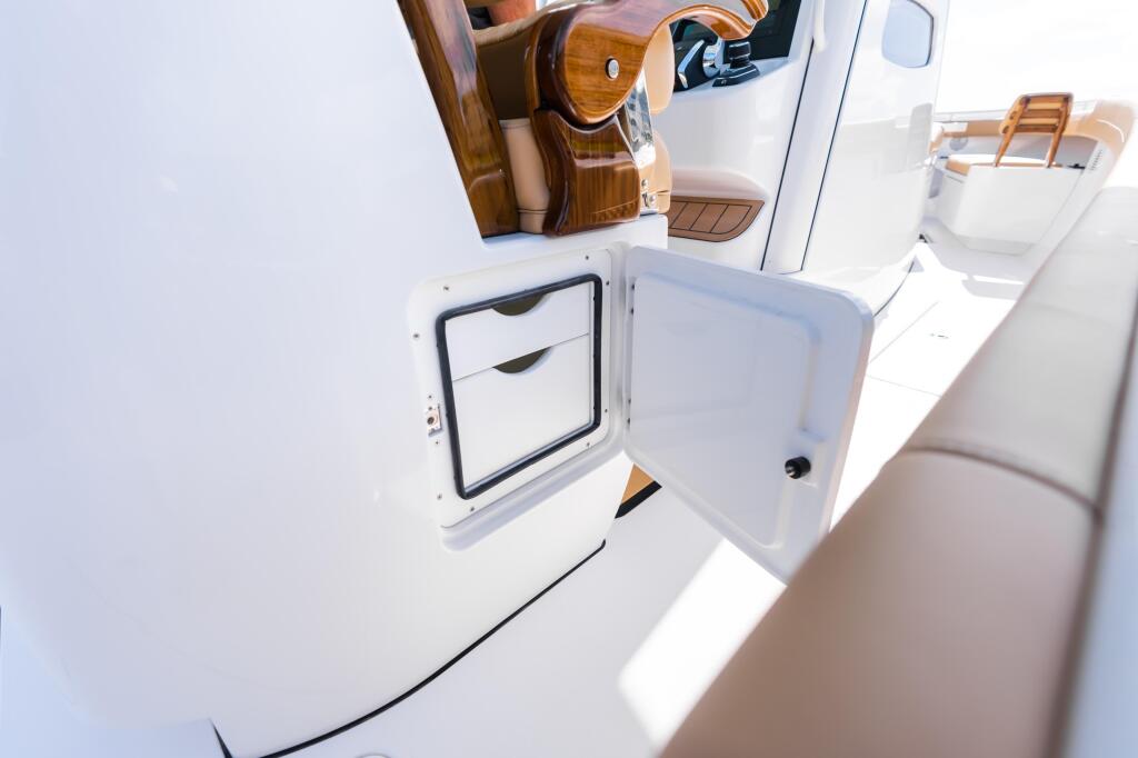 Open white storage compartment on boat deck with wooden helm and seating visible in background