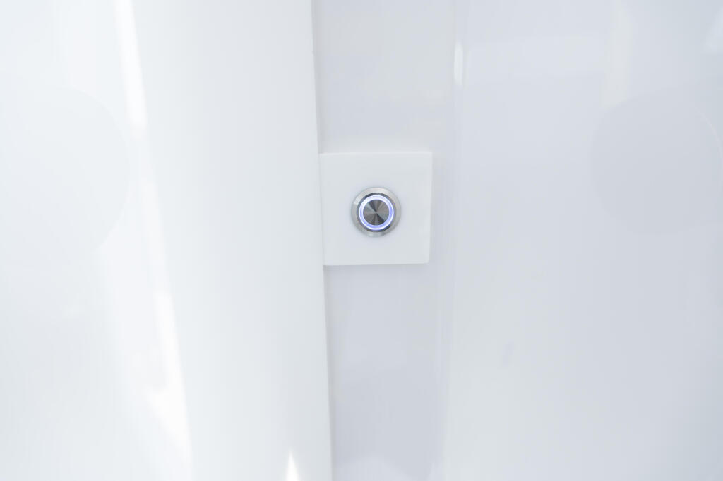 Chrome-trimmed push-button light switch mounted on white cabin wall panel