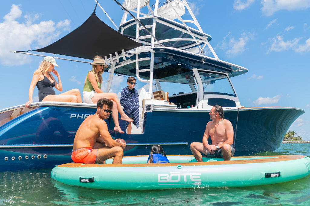 Group of friends enjoying a day on a paddleboard beside a sport fishing yacht with black shade canopy in shallow turquoise water