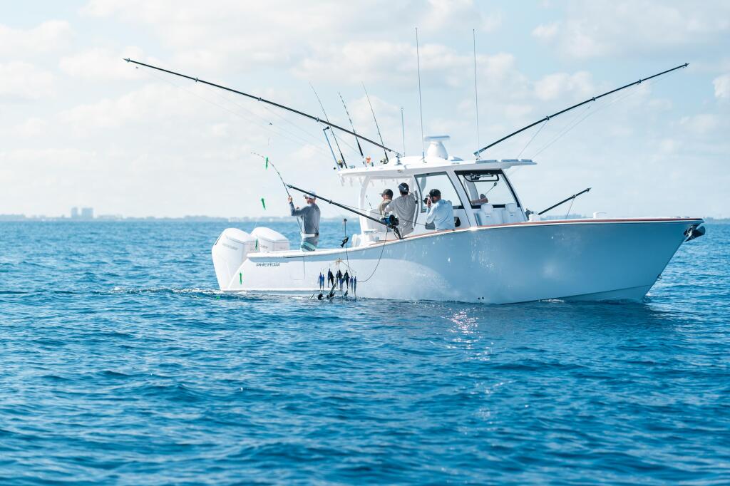 Fishing boat with multiple anglers and outriggers deployed in offshore waters with city skyline visible in distance