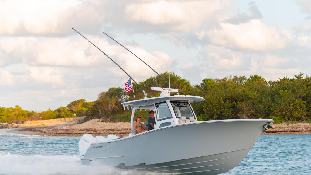 White center console boat with hard-top running through shallow coastal waters near a sandy beach and mangroves
