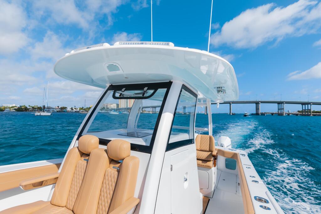 Modern center console boat with tan leather seating and integrated tempered glass windshield cruising offshore past a bridge