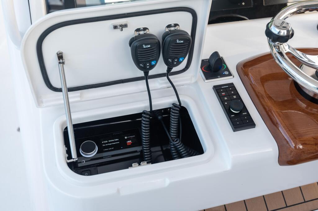 Helm electronics including dual VHF radios, stereo controls, and antenna mounted in white console storage compartment