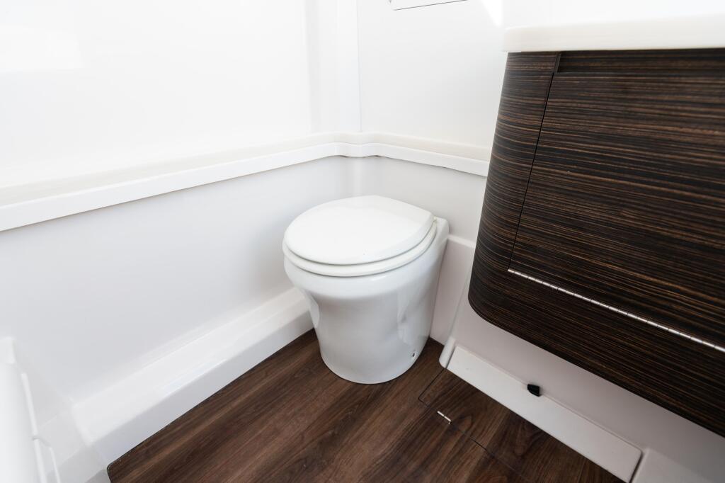 White porcelain toilet with seat in a compact boat cabin with dark wood cabinetry and white walls