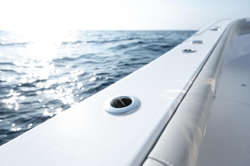 Close-up of a white boat gunwale with a recessed rod holder, ocean and sparkling water in the background