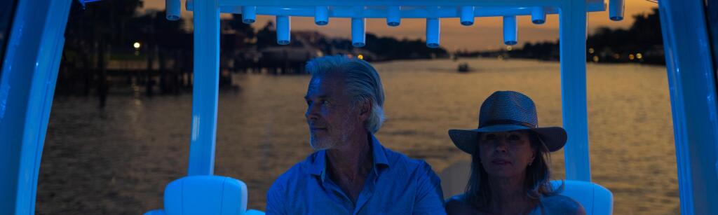 Couple enjoying evening cruise under illuminated hard-top canopy with water view behind
