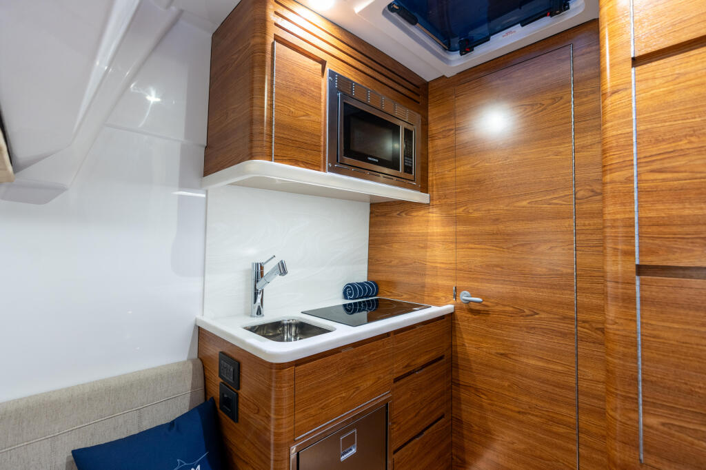 Modern galley kitchen with wood cabinetry, compact stove, and microwave under skylight