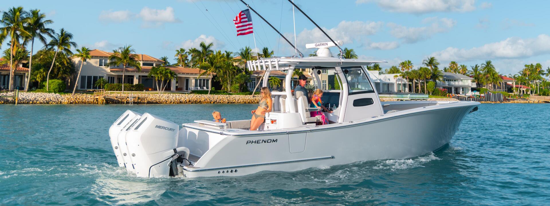 White Phenom center console boat running in turquoise water with families aboard near a palm-lined waterfront community
