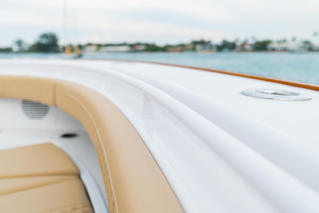 Close-up of boat's white bow railing and tan cushioned seating with waterfront marina in background