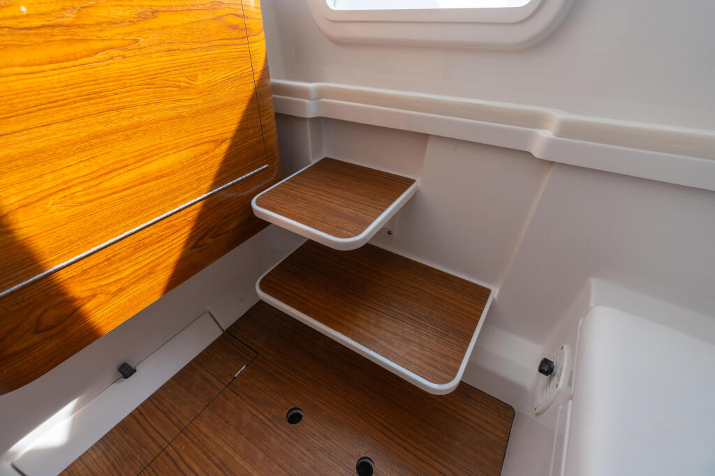 Boat cabin interior with wooden steps, white walls, and bright natural light from porthole window