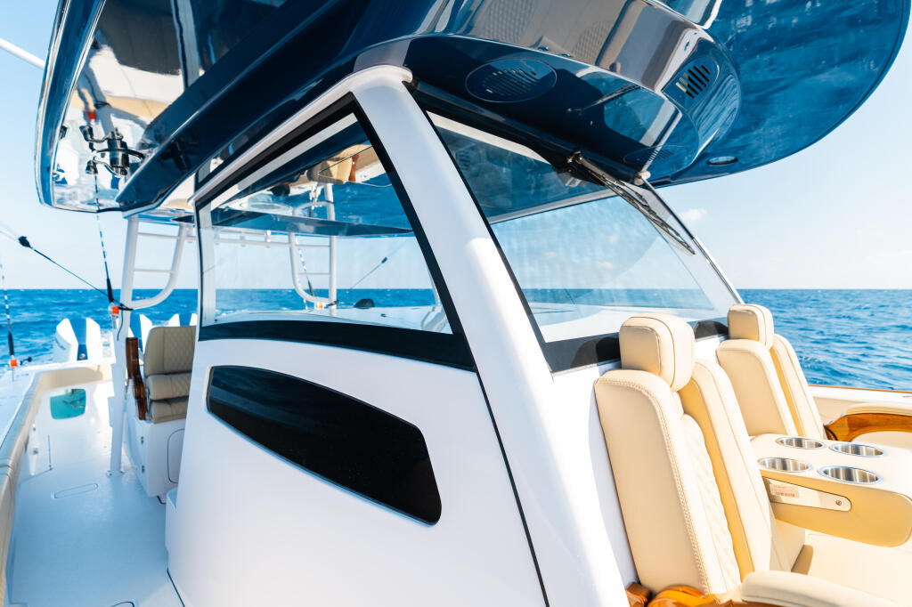 Boat's helm with open hard-top canopy, cream seating, and tempered glass windshield overlooking blue ocean