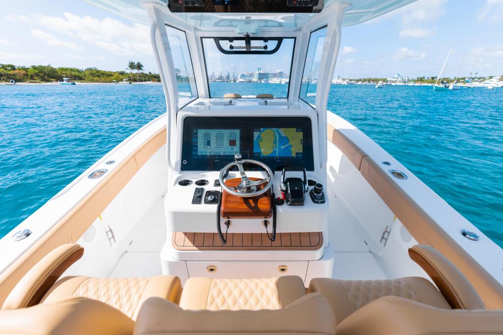 Helm station with dual Garmin displays, steering wheel, and tan seating overlooking turquoise water and distant marina
