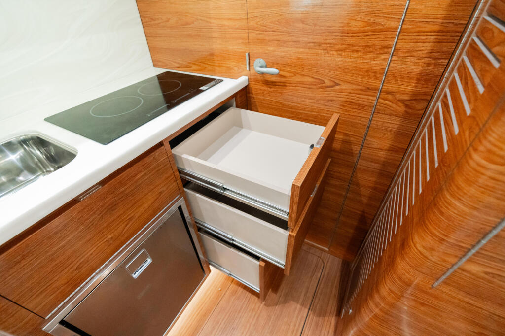 Wooden cabin galley with electric cooktop, sink, and open storage drawers