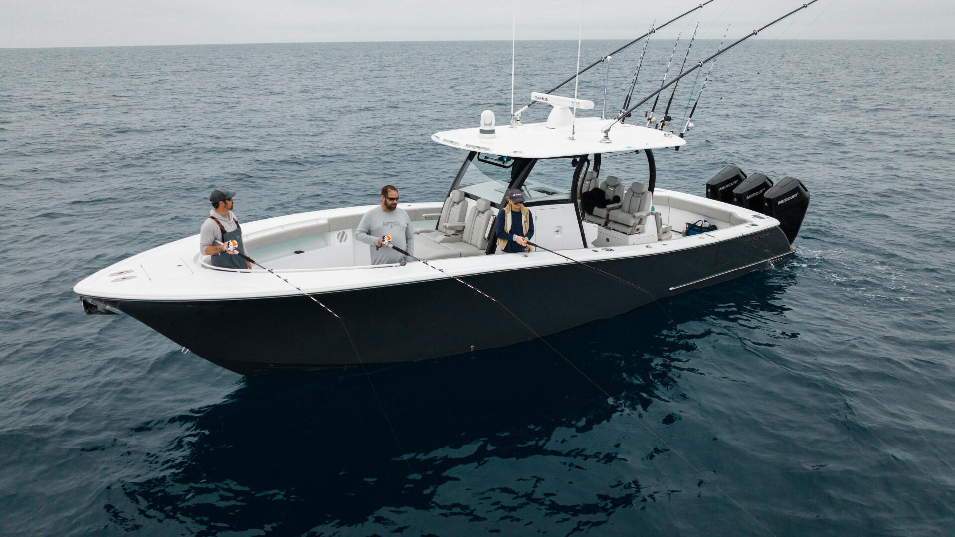 White and black fishing boat with four people and multiple fishing rods anchored offshore in calm blue water, photographed from above