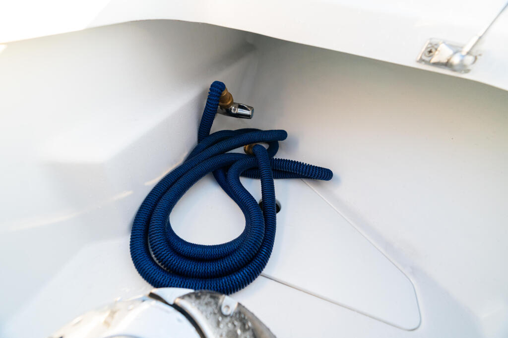 Coiled blue fresh water washdown hose with brass connector mounted in white boat storage compartment