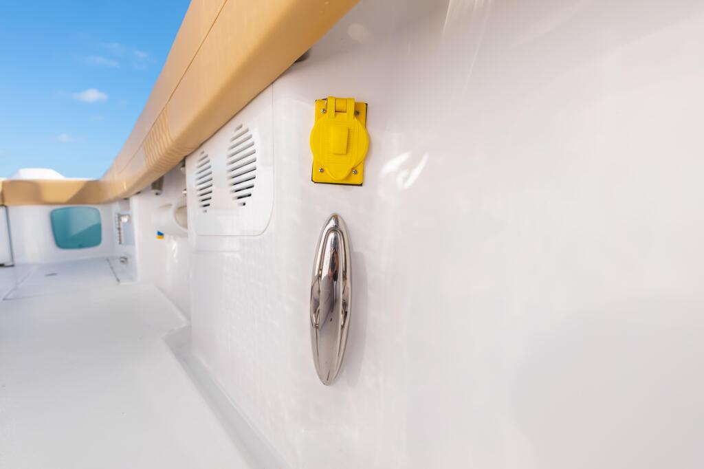Bright yellow electrical outlet mounted on white boat cabin exterior wall with chrome hardware detail