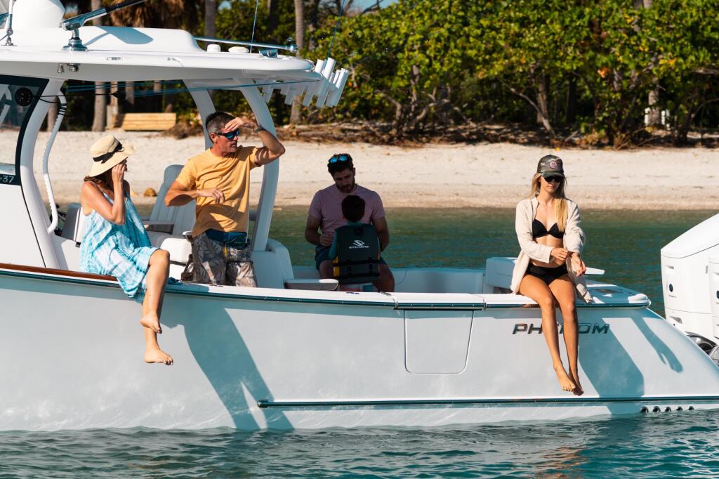 Group of friends relaxing on a center console boat anchored near a tropical beach with palm trees