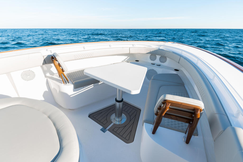 Spacious bow seating area with white upholstered seats, a white table with black pedestal base, and wooden accents overlooking calm blue ocean