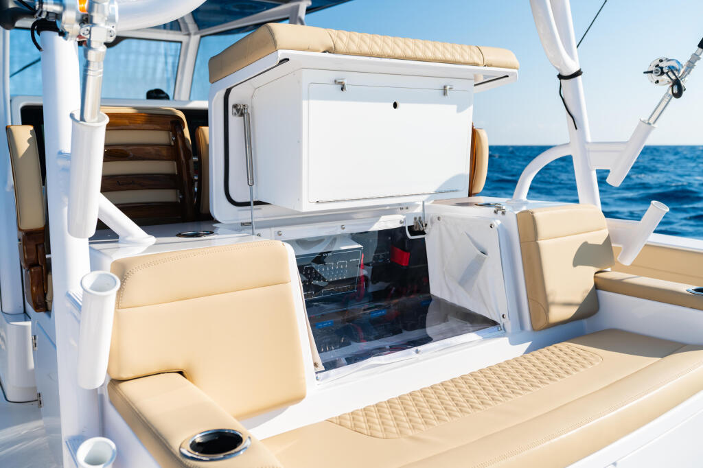 Boat helm station with cream seating, electronics display, and open storage hatch overlooking calm blue water