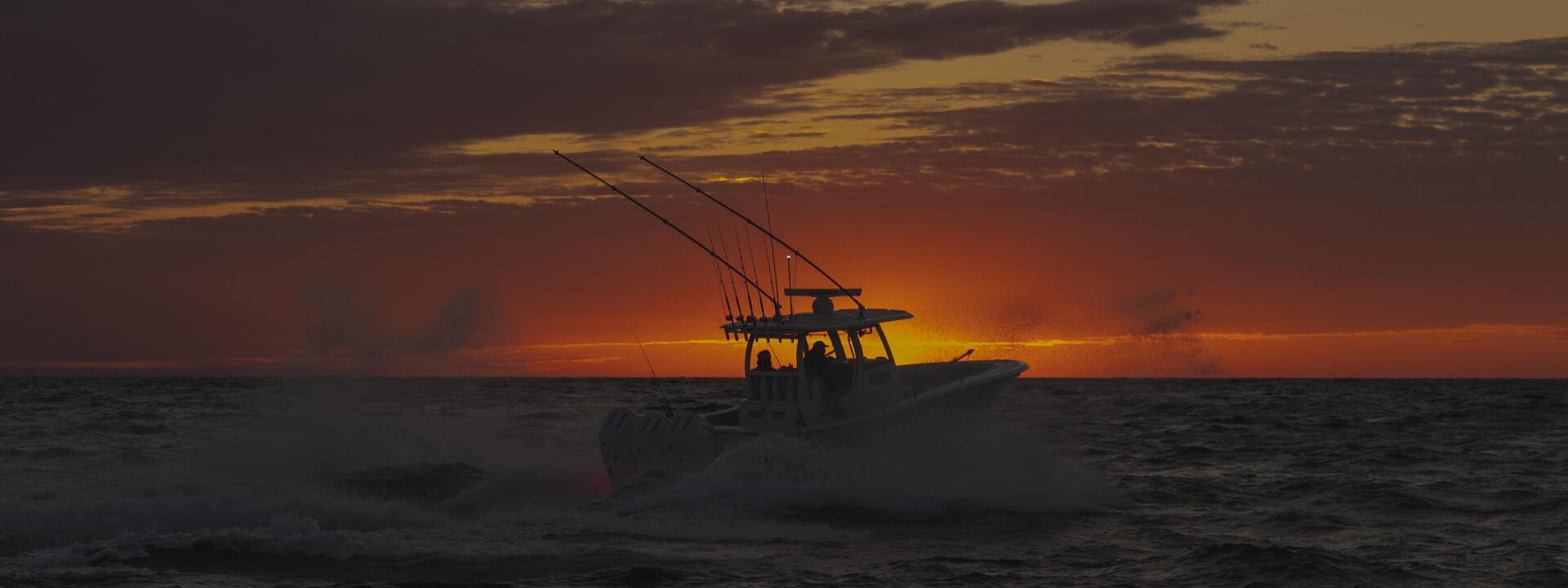 Fishing boat silhouetted against a dramatic golden and orange sunset on the open ocean