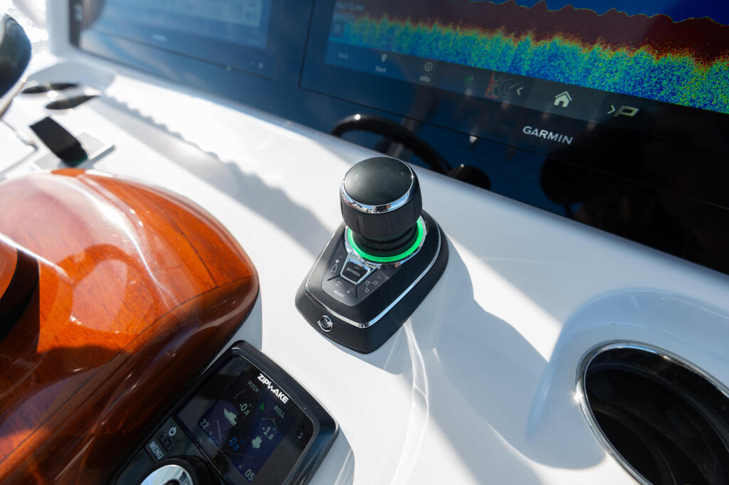 Boat helm station with Garmin sonar display, joystick control, and orange navigation light in bright sunlight