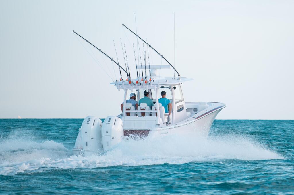 White fishing boat with dual outrigger poles running through ocean waves with crew aboard