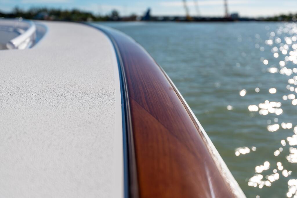 Close-up of boat's white deck and faux-teak toe rail with sparkling water and marina in background