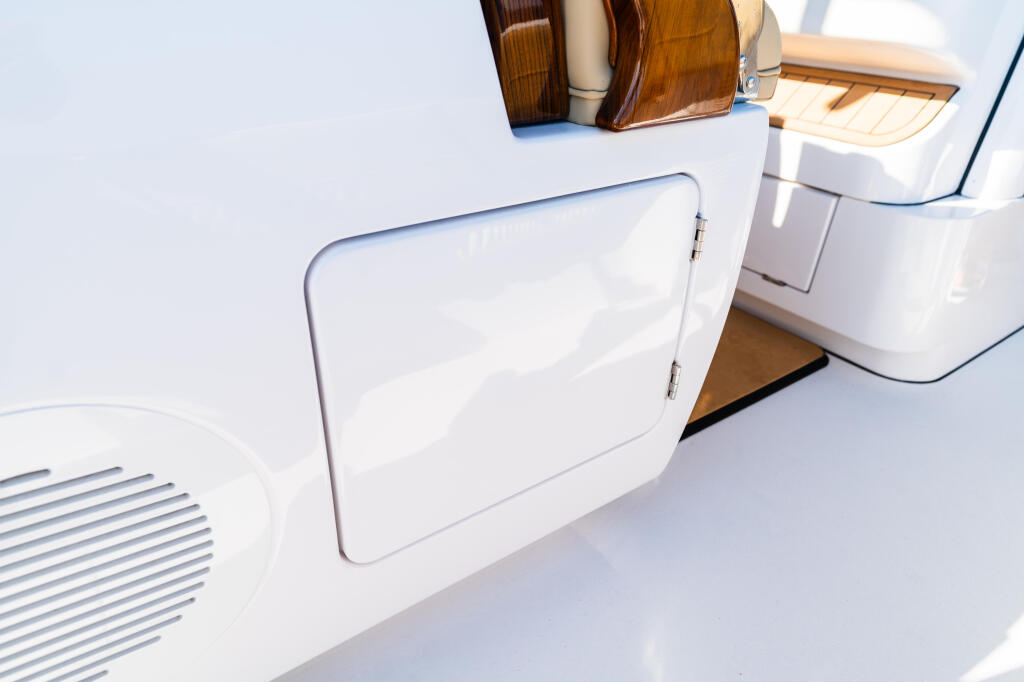 White fiberglass storage compartment with hinged door on boat deck, teak railings visible above