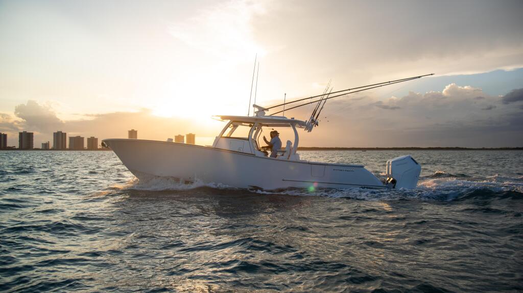 White fishing boat anchored in shallow water at sunset with a coastal city skyline in the background