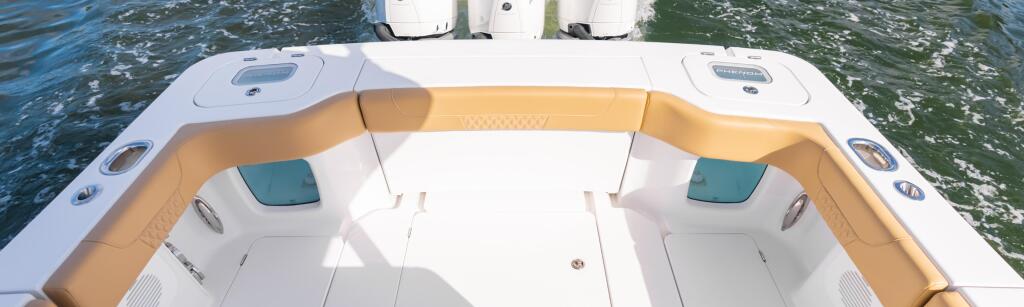 Overhead view of boat stern with tan seating, white deck, and three mounted outboard engines above calm water