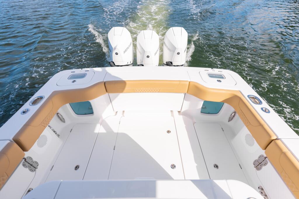 Overhead view of boat stern with tan seating, white deck, and three mounted outboard engines above calm water