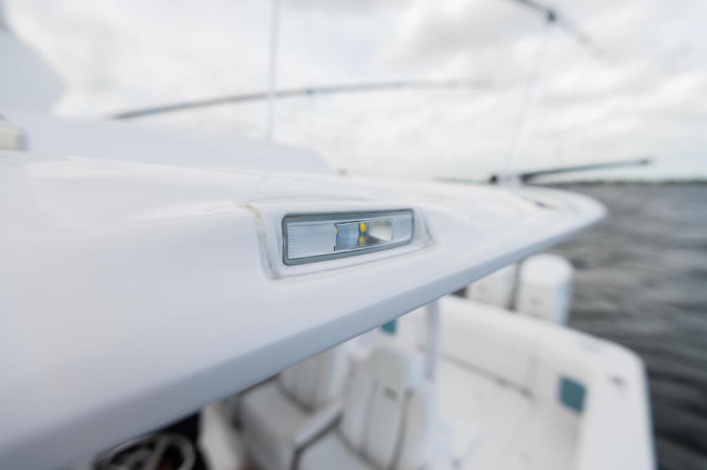 Close-up of a white boat's side spreader light fixture mounted on the gunwale near the helm
