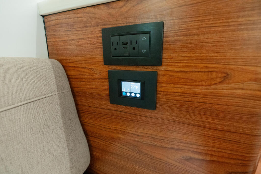 Cabin wall with teak wood paneling featuring power outlets, USB port, and digital control panel with illuminated buttons