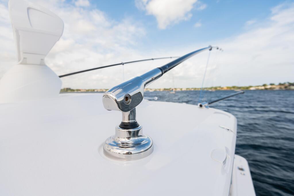 Fishing rod mounted on the rail of a white boat with calm blue water and shoreline in the background