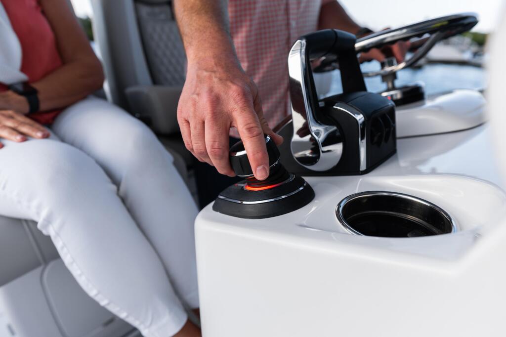 Hand operating joystick piloting system controls at boat helm with cup holders visible