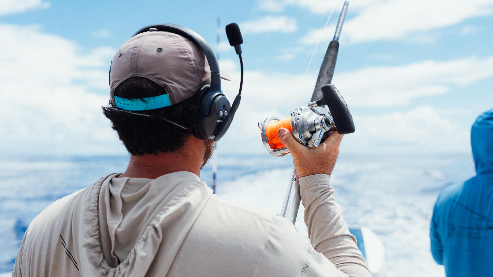 Angler in headset holding chrome and orange fishing reel while facing offshore waters
