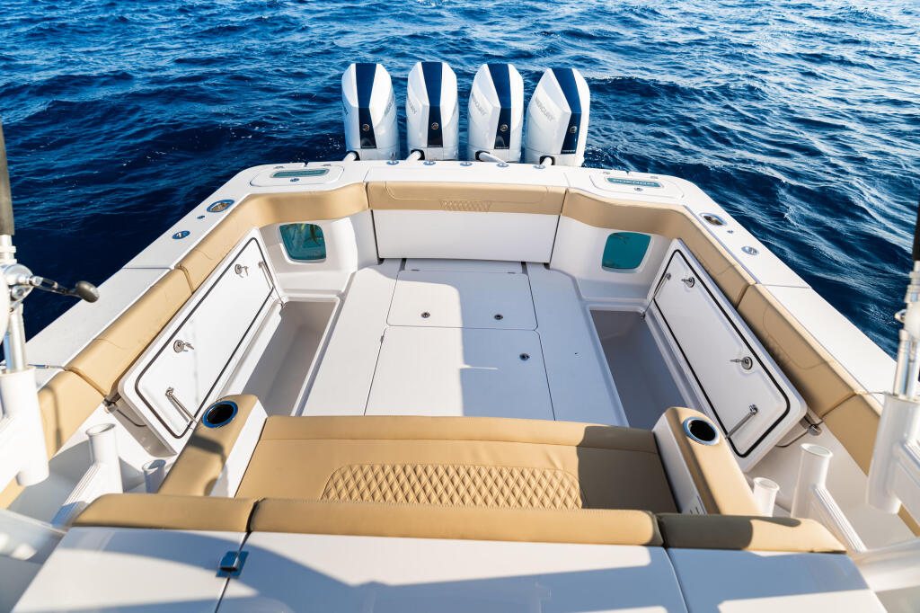 Spacious stern seating area with tan and white upholstery, storage compartments, and five blue-and-white captain's chairs overlooking calm blue water